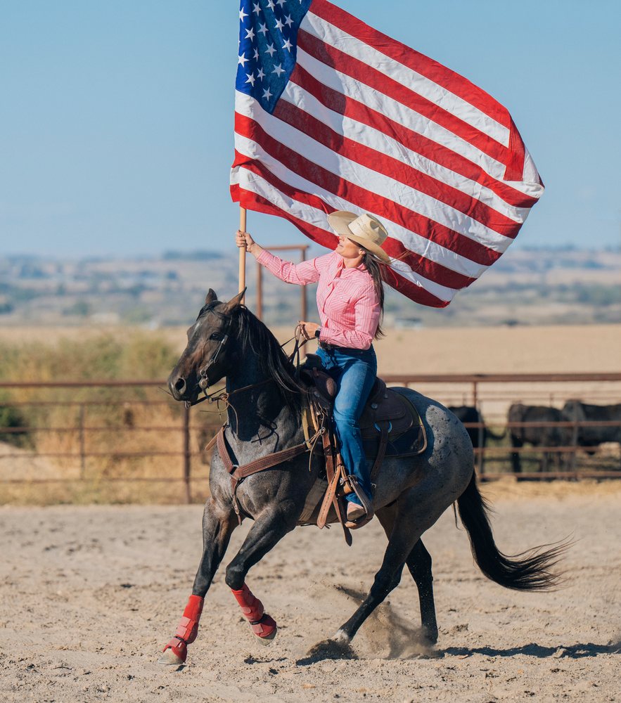 Woman riding horse holding american flag at ranch, Southwest USA.