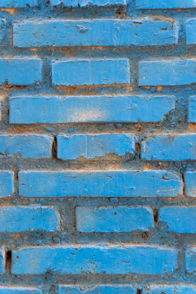 Close-up of a blue painted brick wall in Spain showing rough weathered surface and aged texture, abstract texture, background, wallpaper.