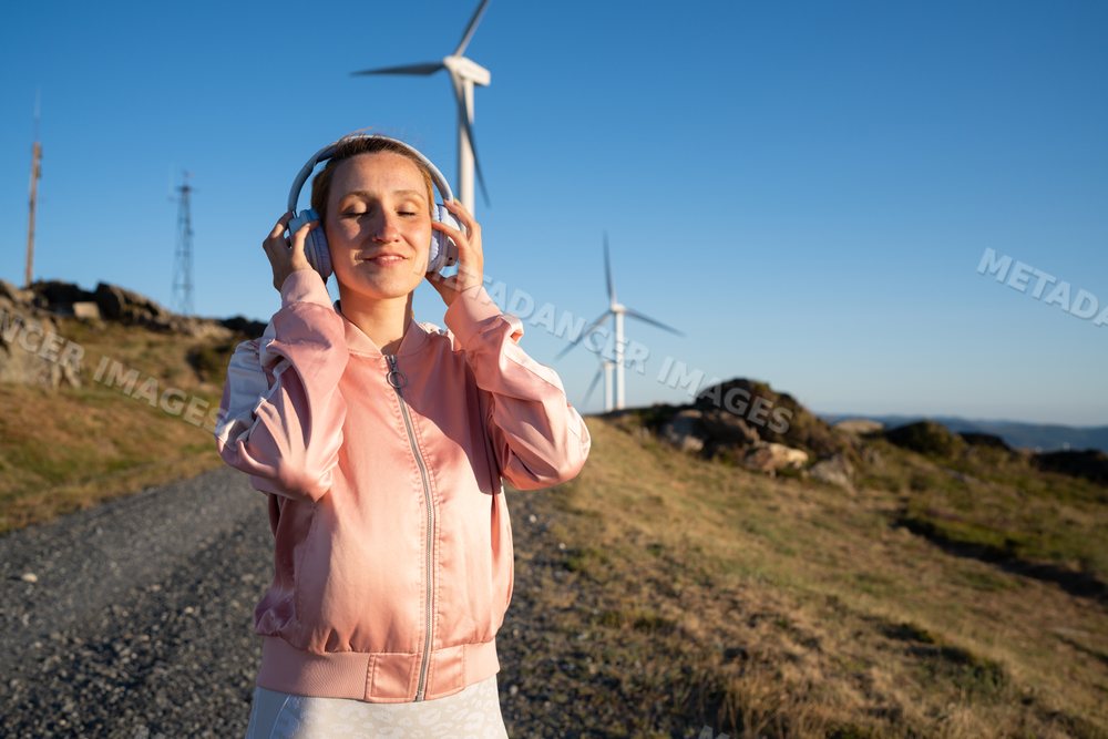 A white woman listens to music near wind turbines in Galicia, Spain