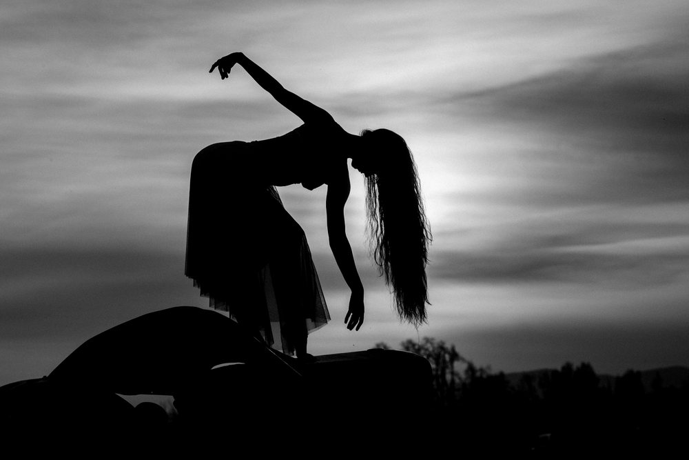 Silhouetted woman in a tulle skirt balances gracefully outdoors at sunset beneath a dramatic sky, USA.