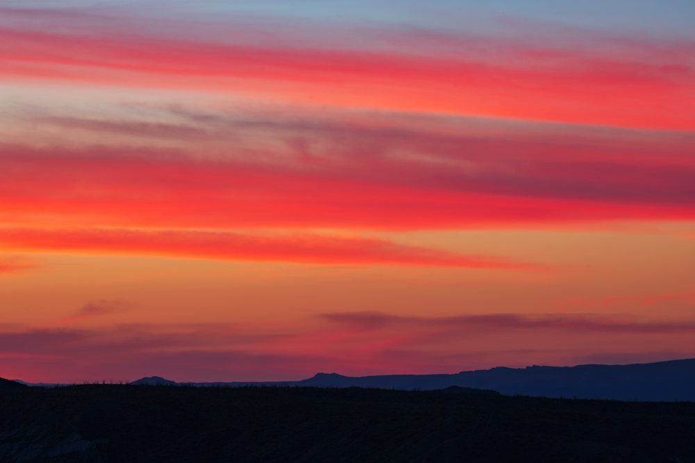 Sunrise with vibrant red and orange clouds over silhouetted mountains in Big Bend National Park, landscape, wildlife, Mule Ears, Texas, USA.