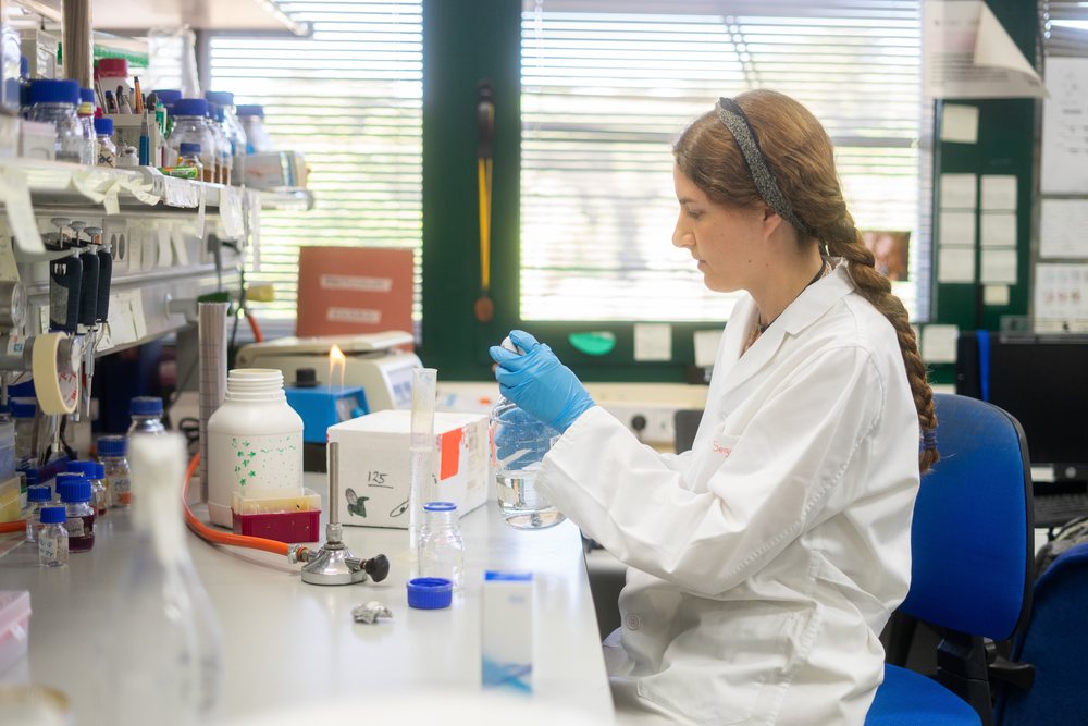 Woman scientist in Seville laboratory working with glass beaker and scientific equipment during research, Andalucía.