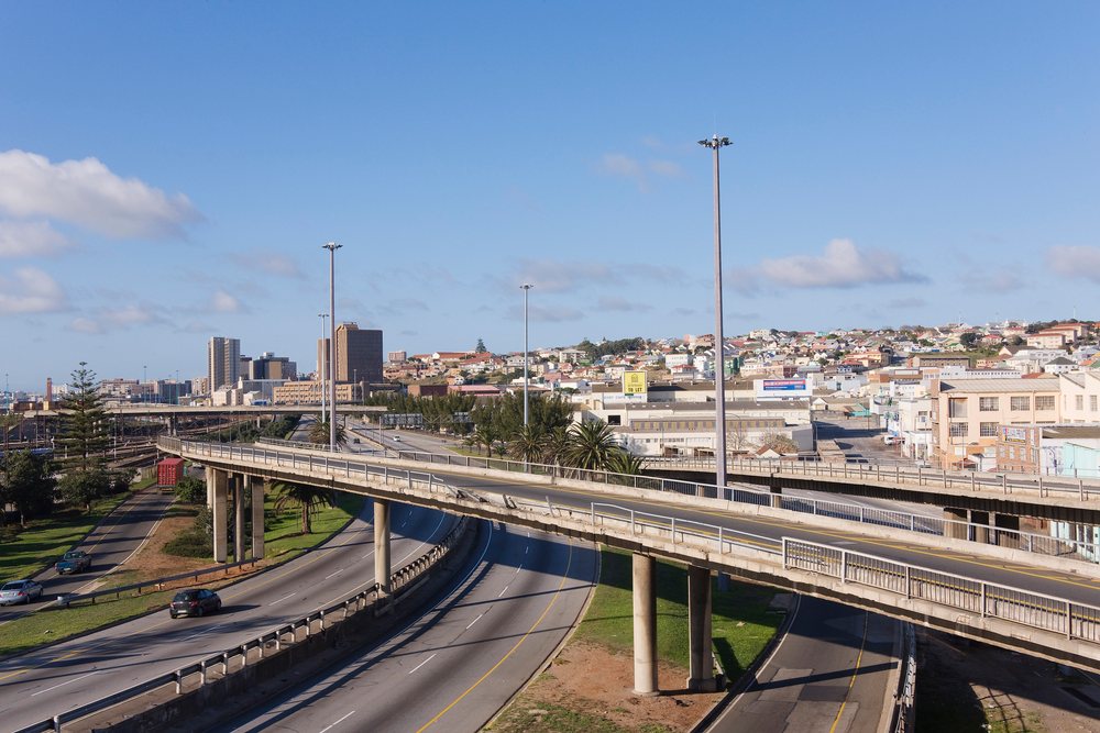 Multi-lane highways and concrete overpasses with cars and streetlights in urban Eastern Cape, South Africa under a clear blue sky.