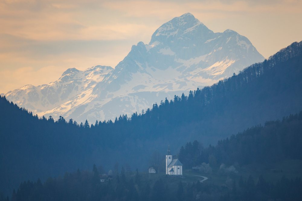 Small church on a hill with snow-covered Mount Triglav, Slovenia at sunset, landscape, cityscape, Skofje Loka, Slovevia.