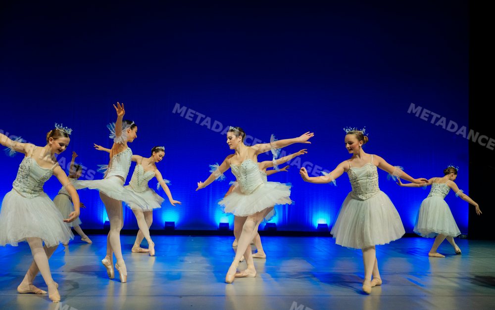 Young ballerinas perform a ballet dance on stage with blue lighting