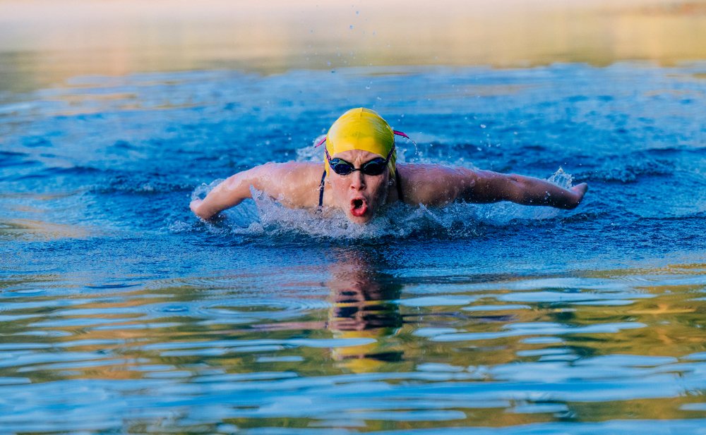 Swimmer wearing a yellow cap performing butterfly stroke in an outdoor swimming pool, USA.