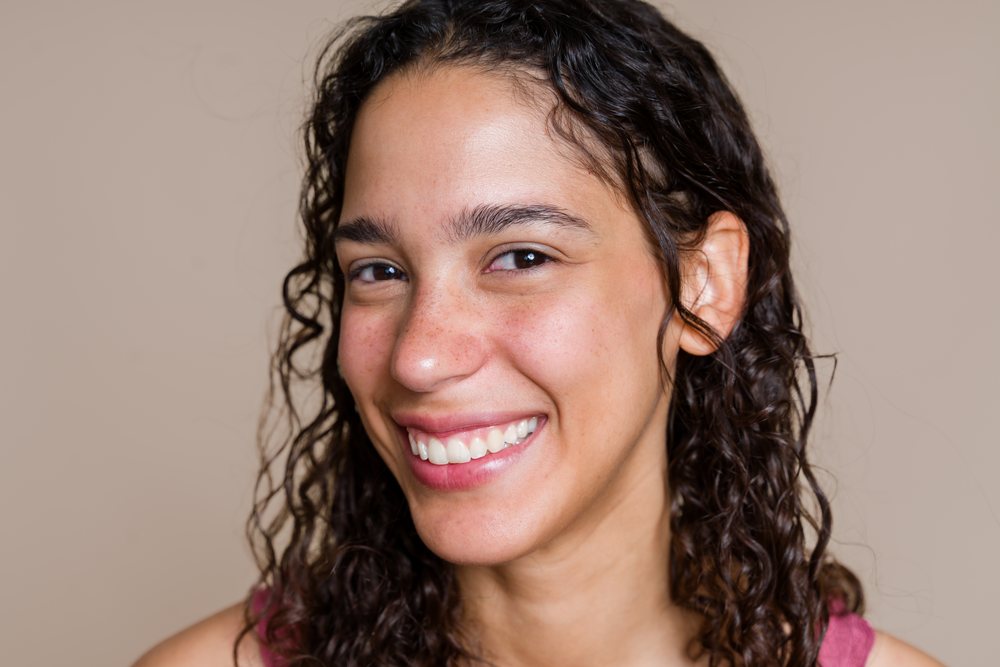 Close-up portrait of a smiling woman with curly hair and freckles against a neutral background, beauty shoot, Spain.