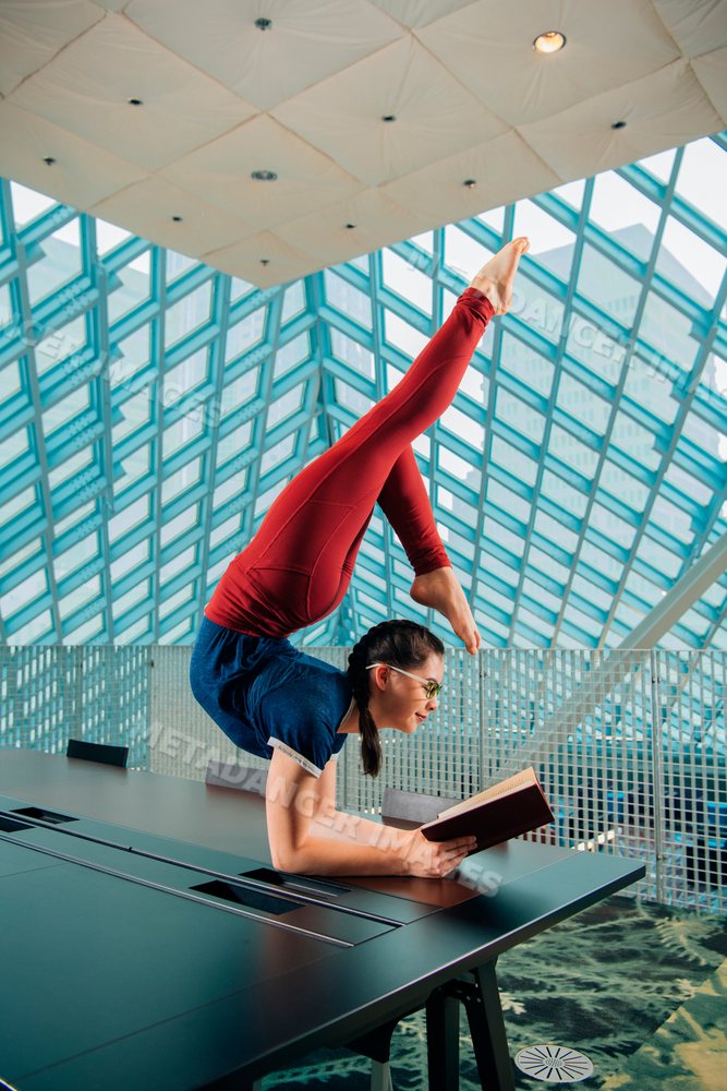 A woman reads a book while doing a handstand in a library