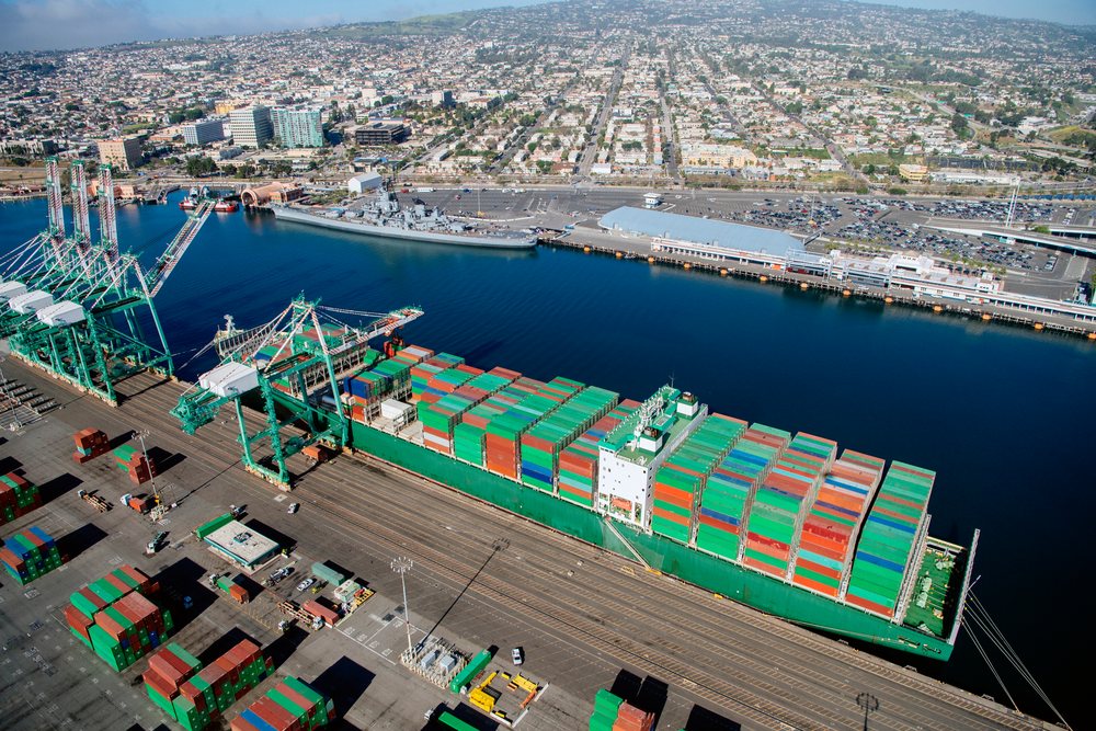 Container ship loaded with shipping containers docked at the Port of Long Beach with adjacent urban area and shipping cranes, CA, USA.