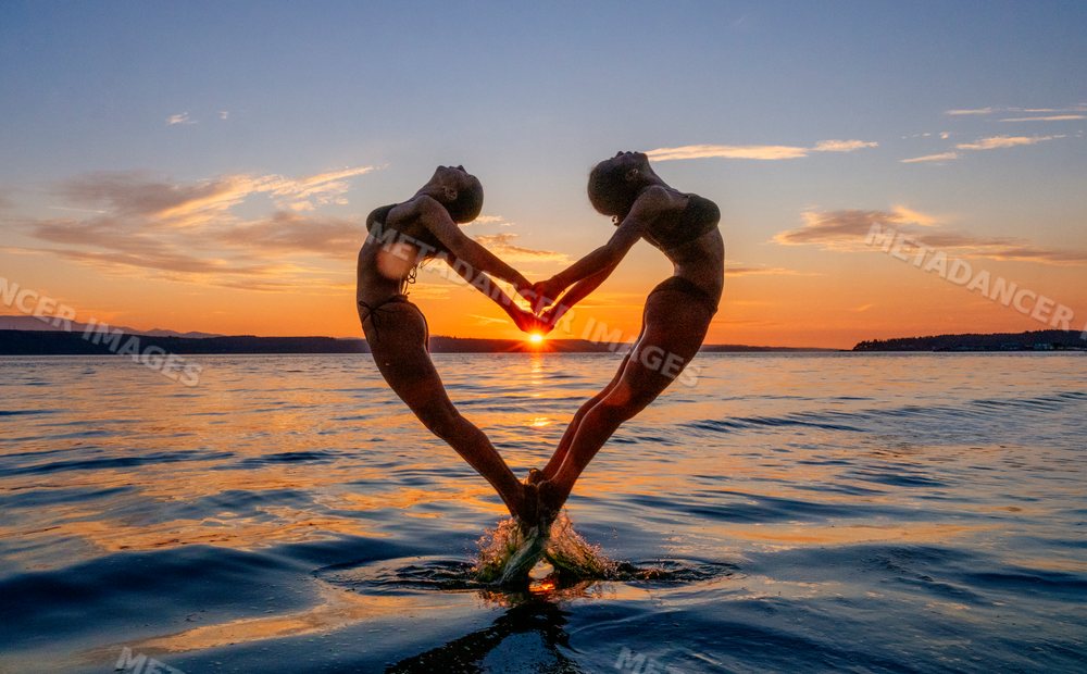 Two women performing partner acrobatics yoga at sunset on water