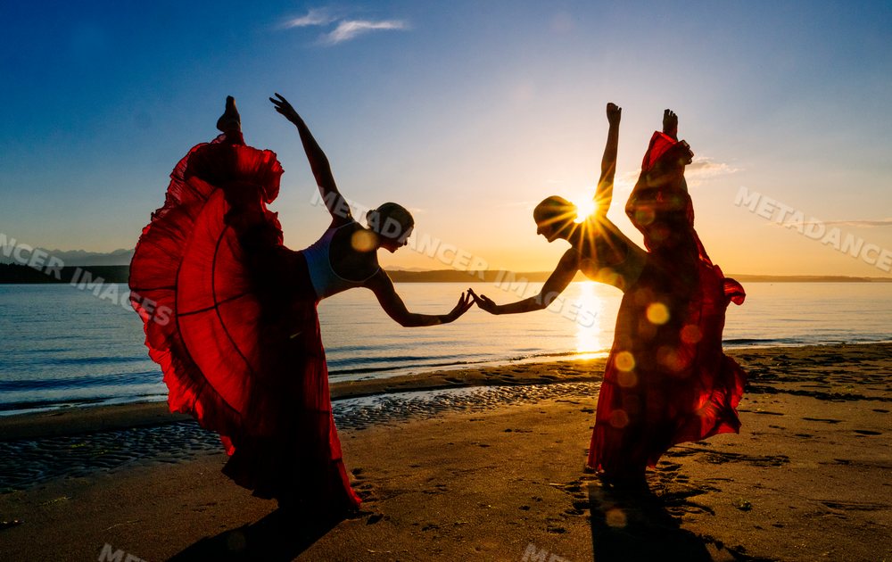 Two white women performing partner acrobatics yoga on a beach