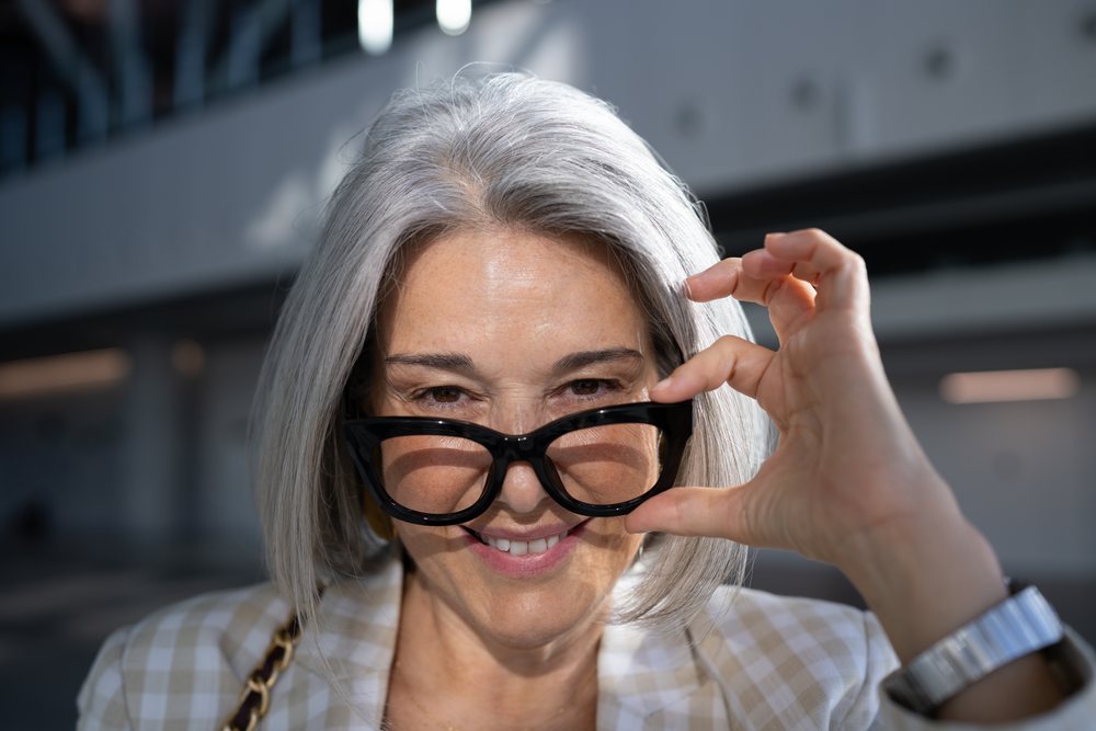 Mature woman with gray hair smiling and adjusting her black eyeglasses outdoors in an urban setting, businesswoman, Spain, Madrid.