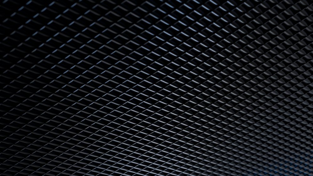 Metal grid ceiling with a triangular pattern creating a repeating geometric texture and light reflections.