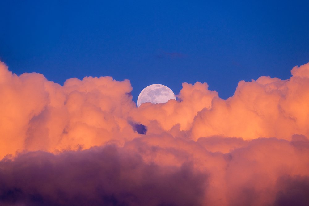 Moon rising above illuminated clouds in a clear blue evening sky over, Seattle, USA.