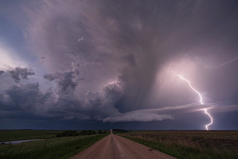 Supercell storm with Lightning striking over a rural dirt road and grass fields at Sunset, Storm Chasing, Weather, Environmental, Jansen, Nebraska, USA.