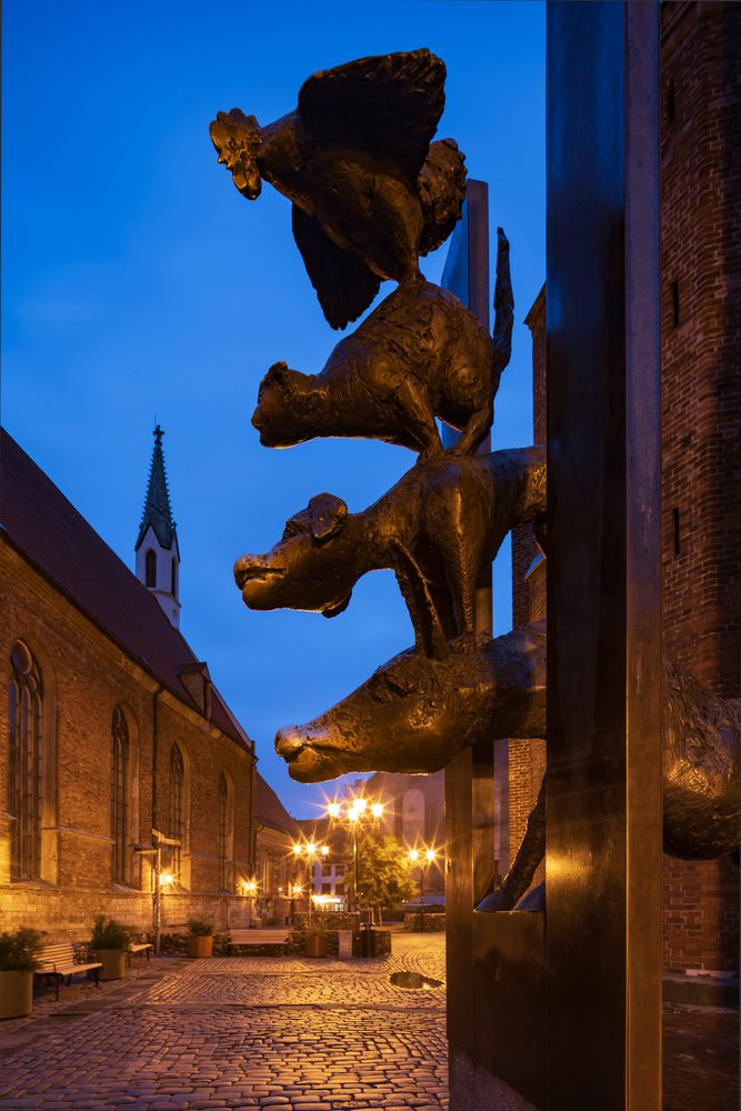Monument to the Musicians of Bremen bronze animal sculptures with dog, cat, and rooster statues on a cobblestone street in Riga at night, cityscape, Latvia, Baltic States.