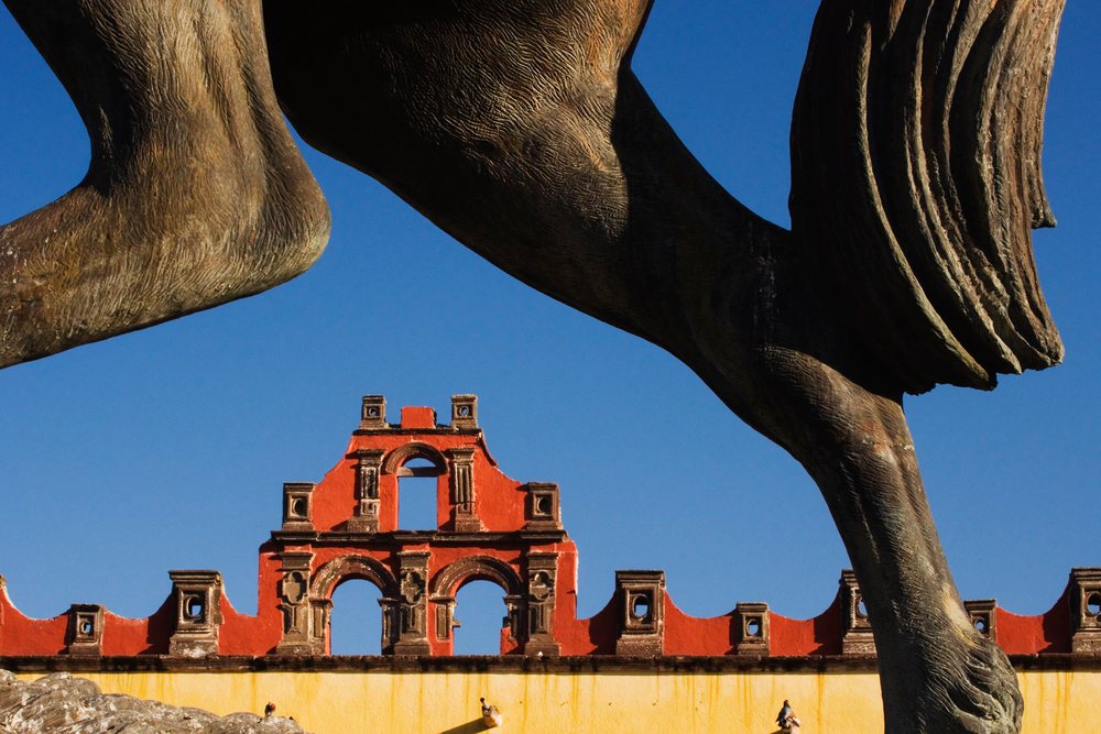 Horse statue legs and tail in foreground with ornate historic building, Guanajuato, Mexico.