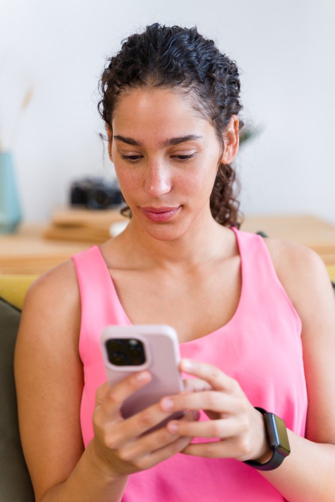 A woman wearing a pink top uses her smartphone indoors, Spain.