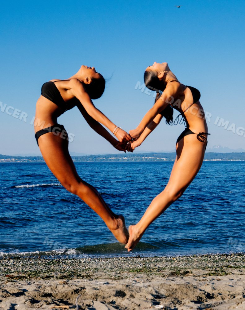 Two women perform a synchronized jump holding hands on a beach