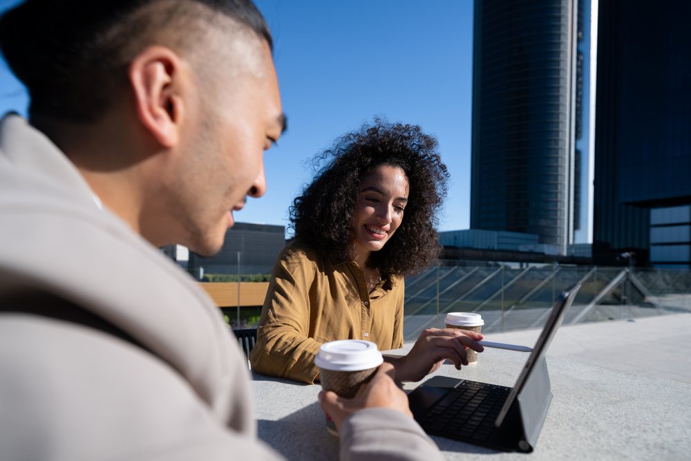 Two people have a business meeting outdoors with coffee cups and a laptop on a table, Madrid, Spain.