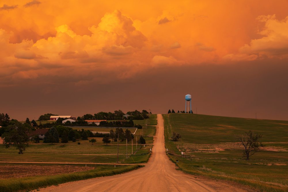 Dirt Road leads toward a water tower beneath a stormy orange sky in the rural countryside, Storm Chasing, Weather, Environmental, Winner, South Dakota, USA.