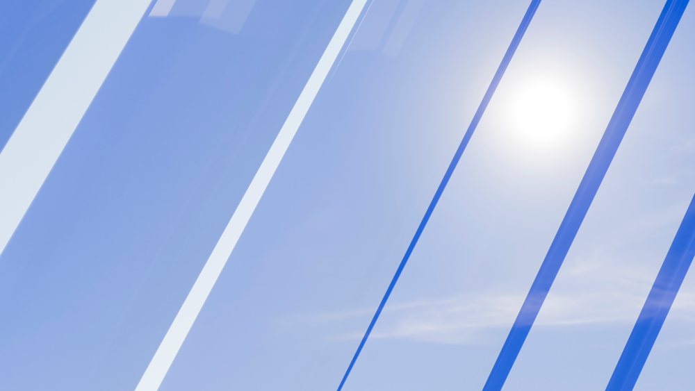 Bright sunlight shines through transparent stripes against a clear blue sky, creating an abstract light pattern.