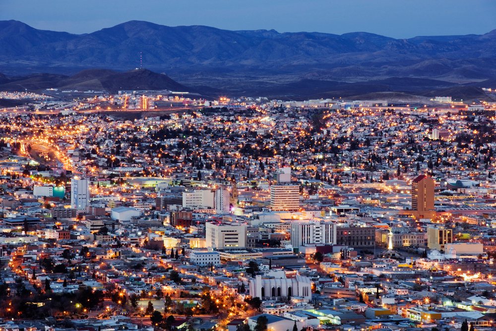 Night cityscape of Chihuahua, featuring illuminated buildings and a mountain range backdrop at twilight, Mexico.
