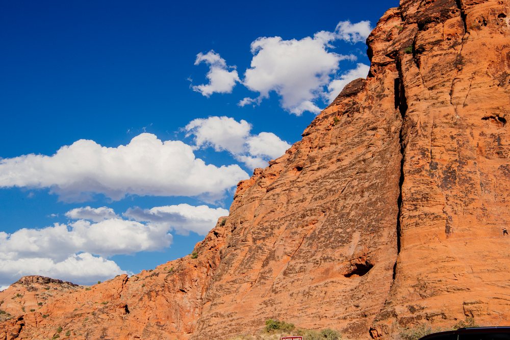Red rock cliffs face under a blue sky with scattered white clouds in red Cliffs Desert State Park, Snow Canyon, Utah, USA.