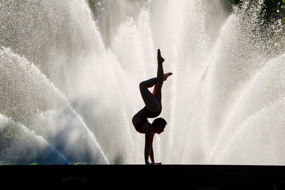 Female gymnast performs a handspring silhouette outdoors in front of a water fountain, USA.