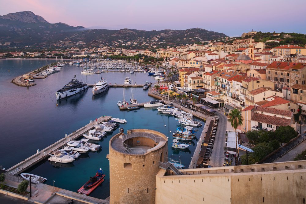 Dawn view of Calvi Harbour with boats docked at the marina and the historic Citadel overlooking the coastal village, Travel Photography, Corsica, France.