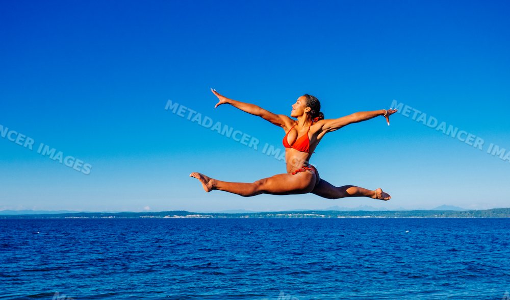 Woman in red swimwear jumping over ocean water on a clear day