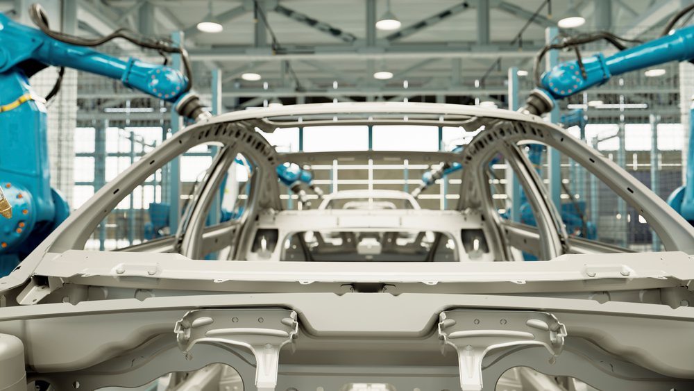 Robotic arms operate around a metal car frame on an assembly line inside a manufacturing factory.