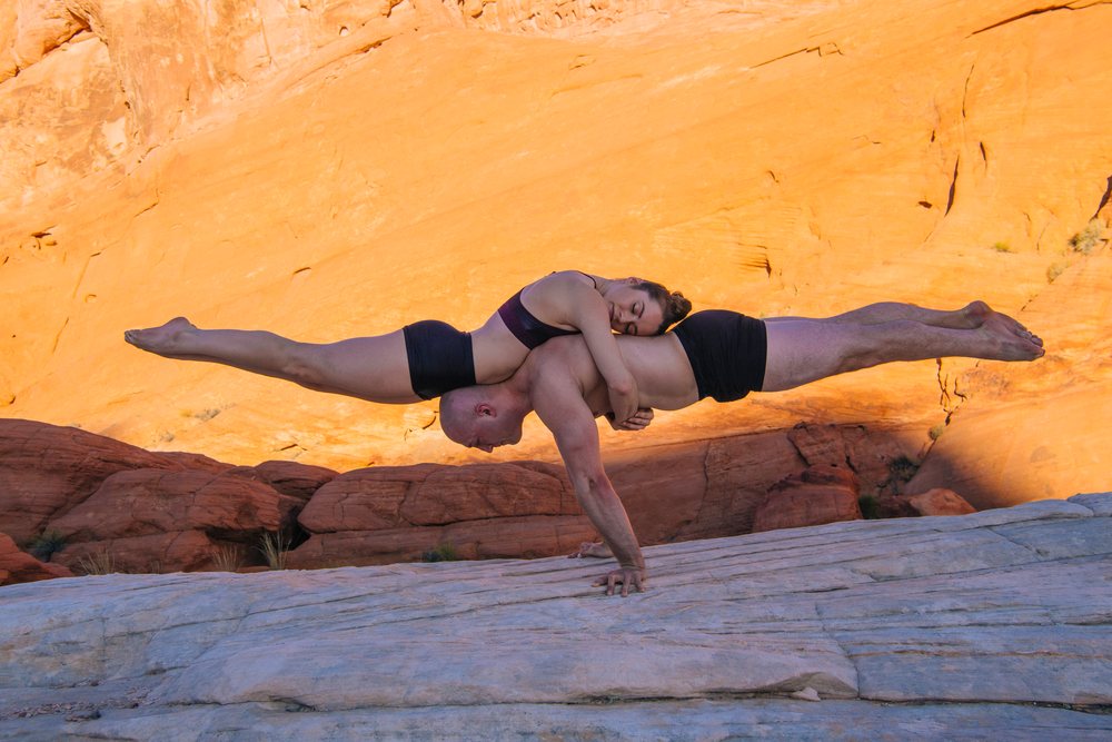Two people perform an acrobatic partner yoga balancing pose barefoot on rocks in a natural desert landscape, USA.