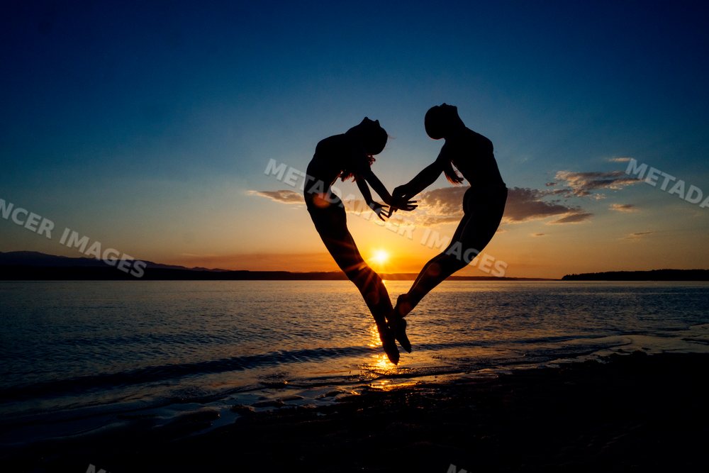 Two white people perform partner yoga acrobatics together