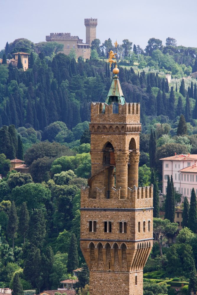 The tower of the Uffizi Gallery rises above trees and buildings, topped with a golden weather vane, Florence, Italy.