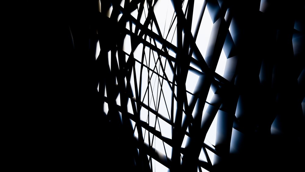 Abstract image of intersecting black lines with light shining through, creating geometric shadows and patterns.