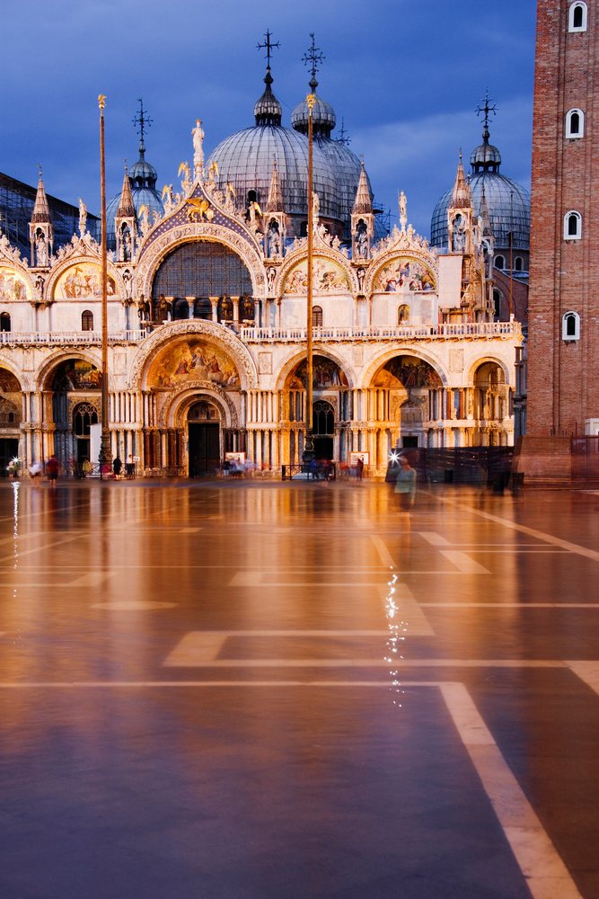 St Mark's Square cathedral illuminated at evening in Venice with tourists visiting the plaza, Veneto, Italy.