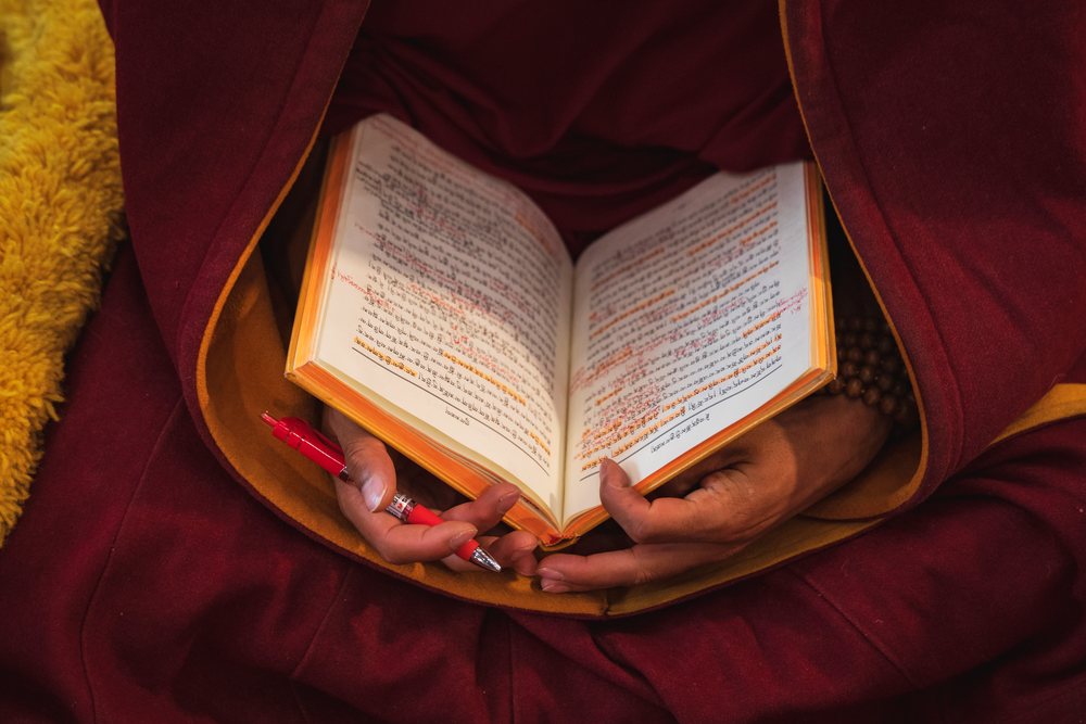 Monk wearing red robe studies annotated Buddhist text indoors at Sexusi Monastery in Kham Tibet, China, Sichuan Province, People's Republic of China.