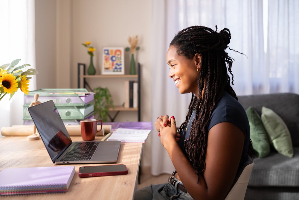 A woman smiles while engaging in an online video call at her home office desk, remote work, student, Spain.