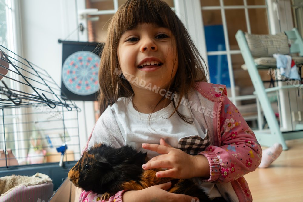 A smiling white girl holding a guinea pig inside a home in Madrid