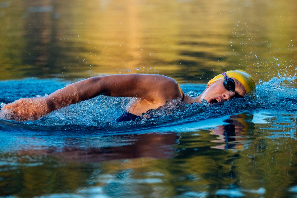 Female swimmer wearing a yellow swim cap and goggles performing a freestyle stroke in open water, USA.