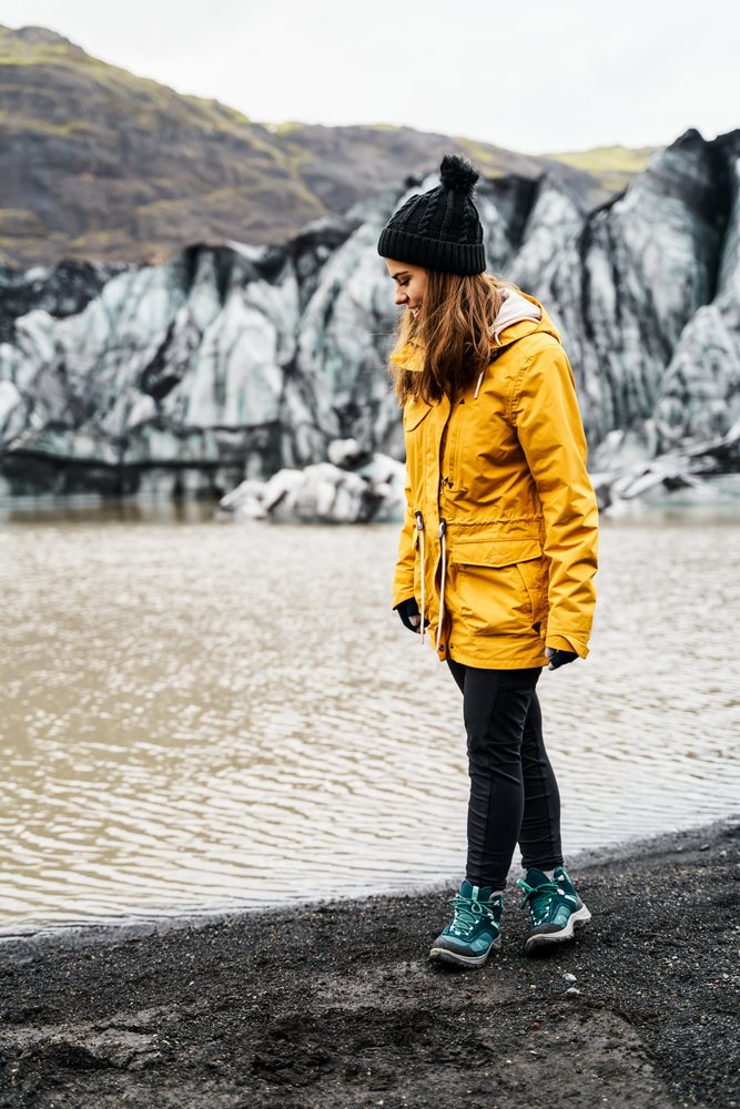 A white woman stands by a lake with a glacier and mountains