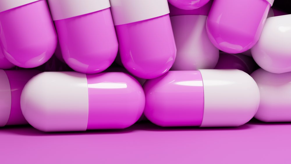 Stacked medication capsules with white and pink halves on a pink background.