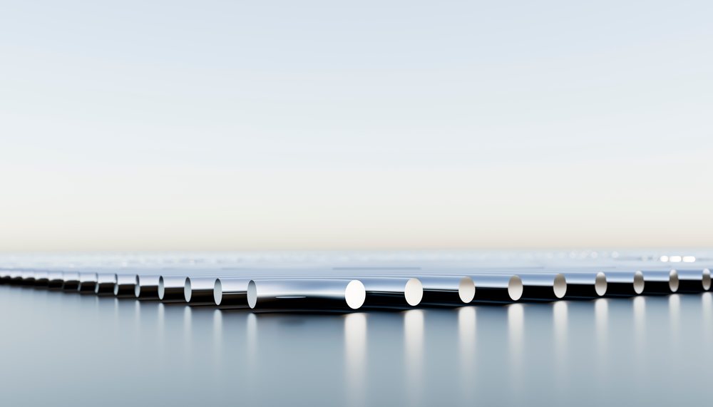 Chrome metal tubes arranged horizontally on a reflective surface in a modern industrial setting.