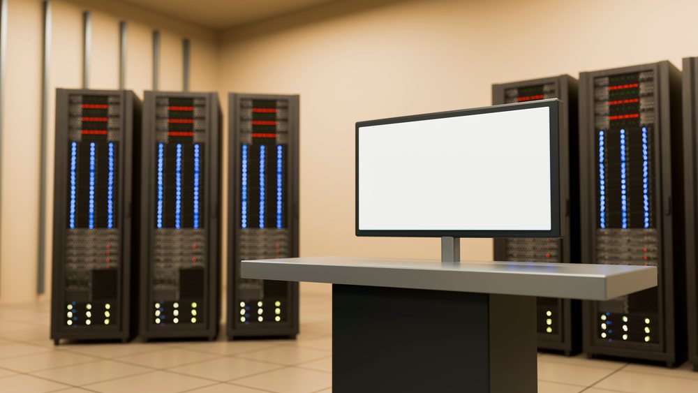 Data center room featuring server racks with illuminated indicators and a blank monitor screen on a metallic console table.