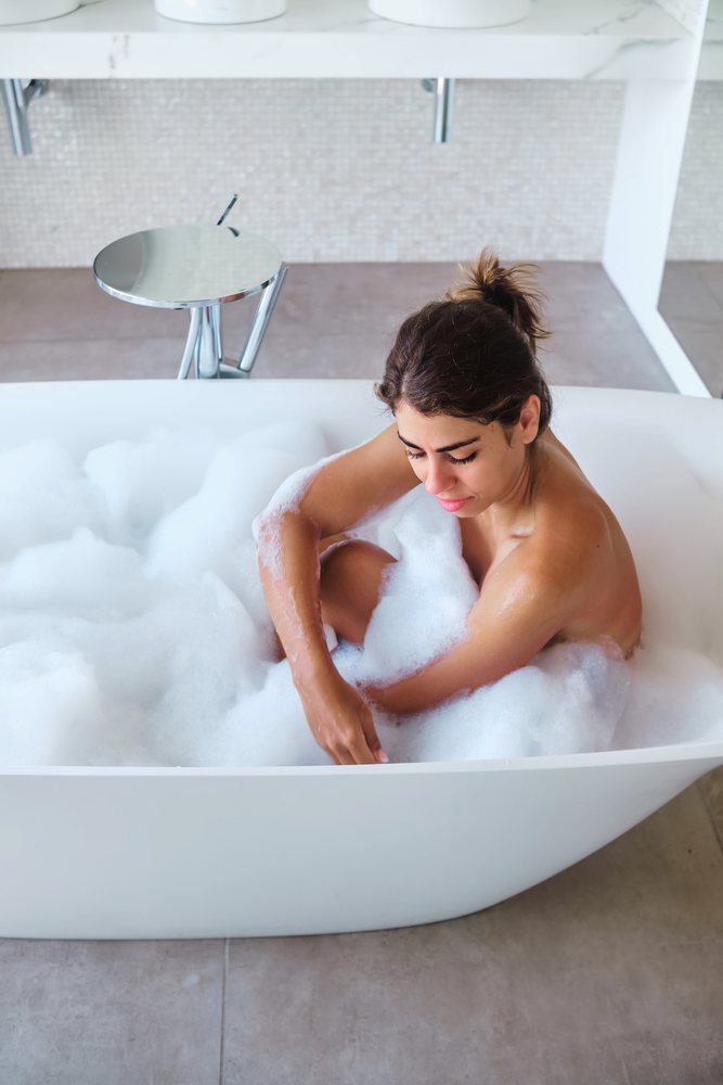 A young woman enjoys a relaxing bubble bath in a modern white bathtub in a bathroom located in the, Maldives.