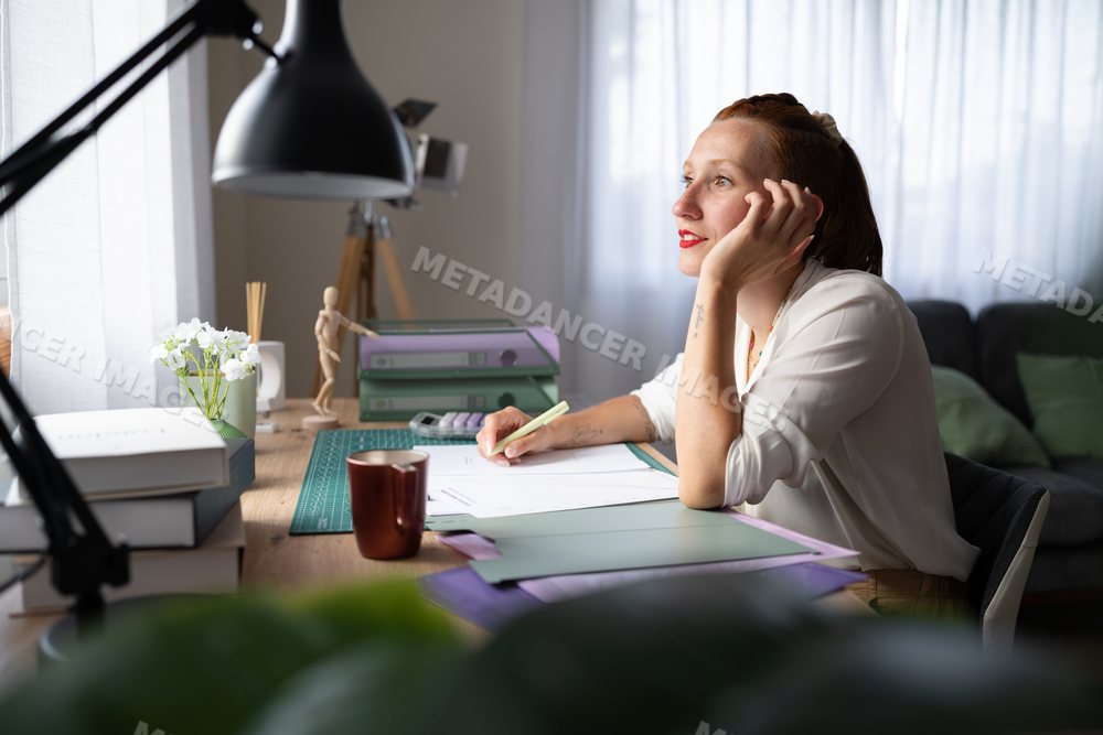 A white woman writing thoughtfully at her home office desk in Galicia