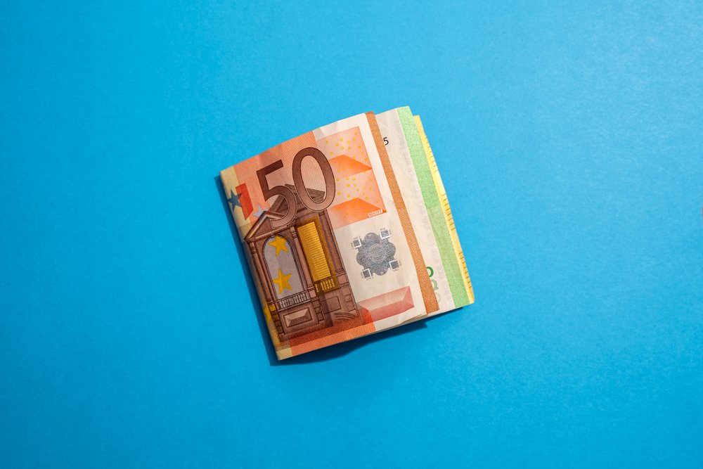 Stack of euro banknotes including 50 euro and smaller denominations lying on a blue surface representing cash and financial transactions.