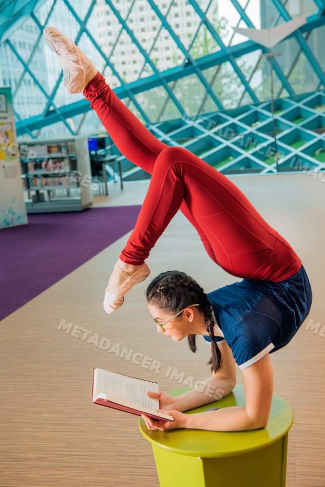 Young woman reads a book while doing a flexible yoga pose in a library