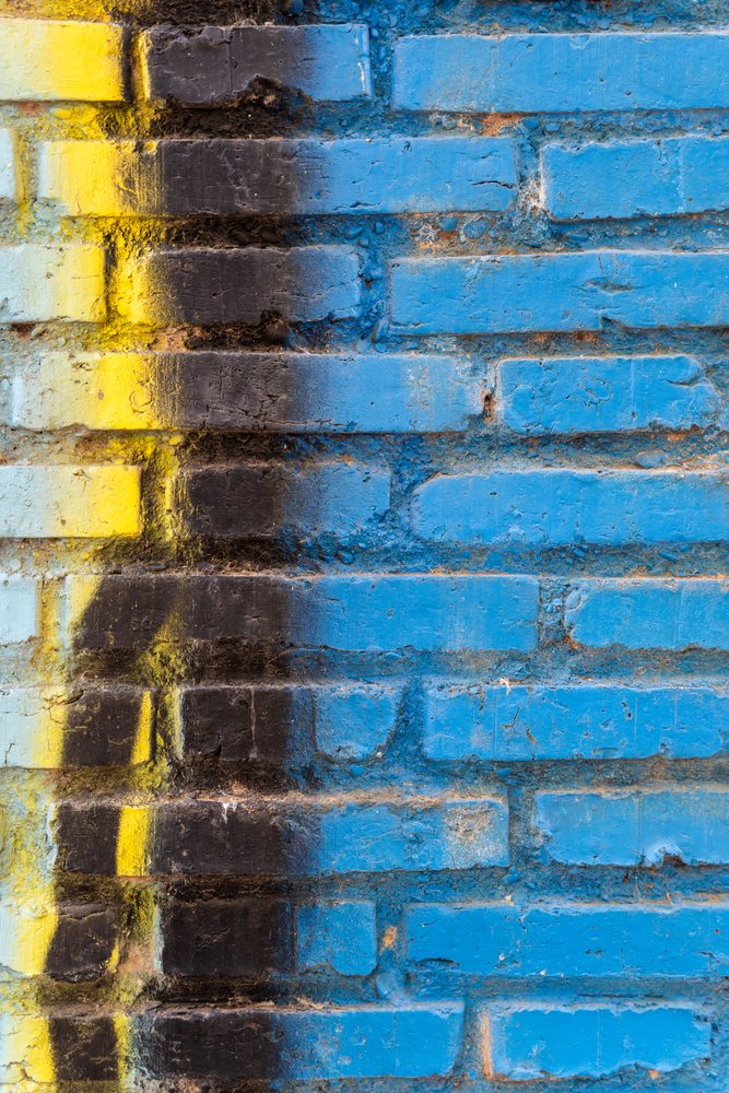 Blue brick wall with yellow and black weathered paint textures showing rough masonry detail, texture, abstract texture, background, wallpaper, Spain.